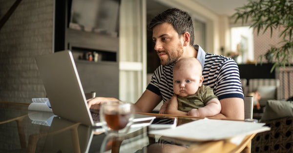 A man working at a laptop with his infant on his lap.