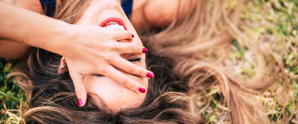 A woman laying in grass with her hand over her face.