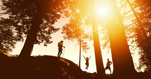 woodland at sunset with two people hiking and girl jumping in the air
