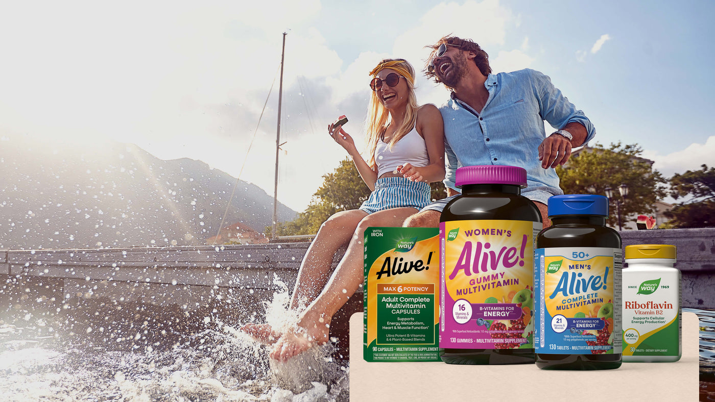 A lifestyle shot of a couple sitting on the edge of a boat with water splashing, with several dietary supplement bottles from Alive! in the foreground.