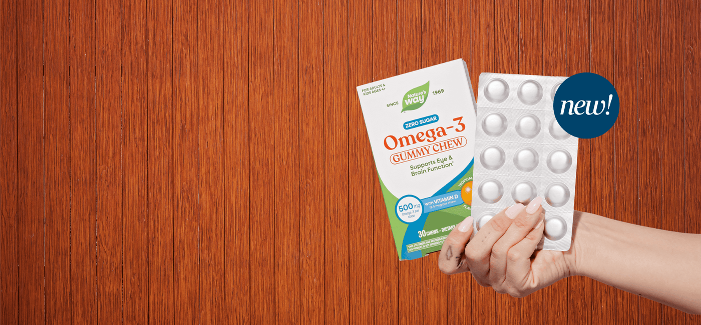 Hand holding a package of Omega-3 gummy chewables with a 'new!' label on a wooden surface.