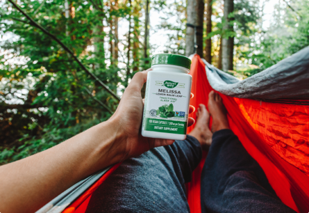 <{%DETAIL1_14650%}>A person laying on a hammock in the woods holding a bottle of Melissa Lemon Balm Leaf.