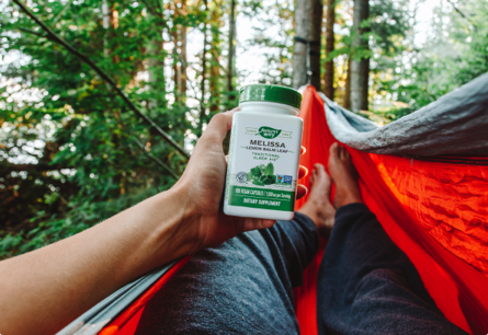 A person laying on a hammock in the woods holding a bottle of Melissa Lemon Balm Leaf.