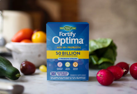 <{%DETAIL1_10762%}>A package of Fortify Optima Adult 50 Plus Daily Probiotic surrounded by fruits and vegetables.