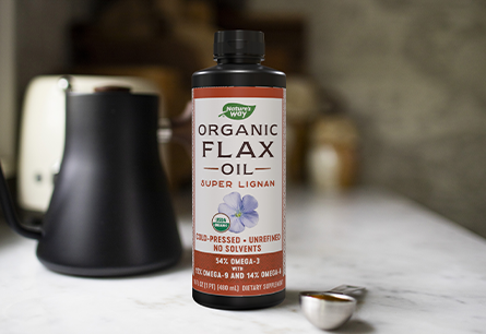 A 16-ounce bottle of Nature's  Way Organic Flax Oil on a marble countertop next to a tablespoon measuring spoon of coffee.