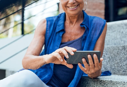A smiling woman sitting on steps outside watching something on her phone.