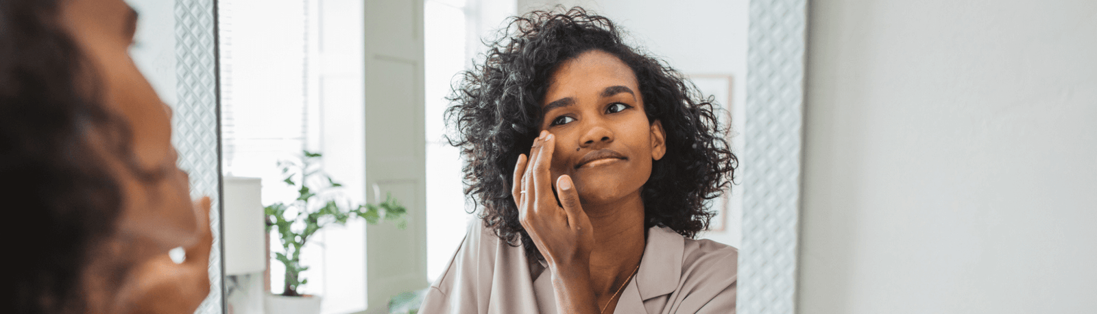 woman looking at face in the mirror, touching her skin