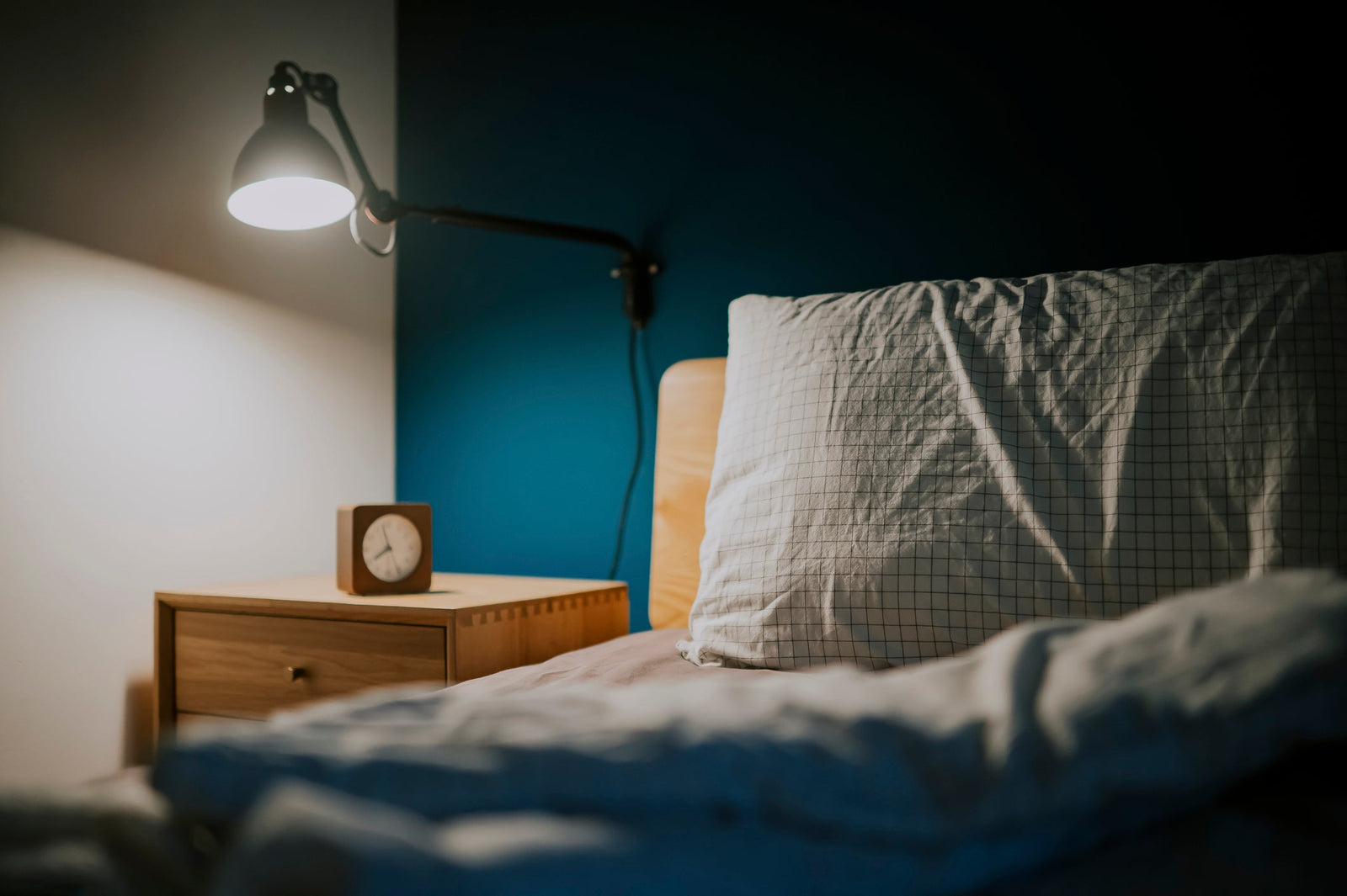 bed with a turned down sheet and a pillow next to a nightstand with an overhead light