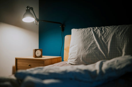 bed with a turned down sheet and a pillow next to a nightstand with an overhead light