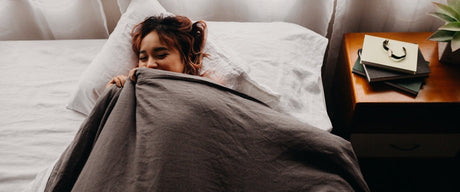A woman sleeping on her back in bed with a blanket pulled up to her face.