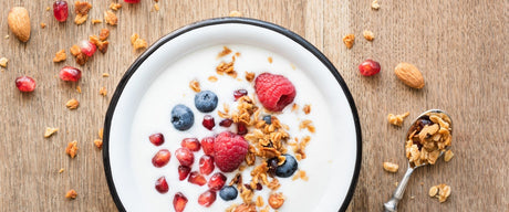 A bowl of yogurt with granola and fruit sprinkled on top and around the bowl.