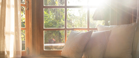 The sun shining through a window onto 3 white throw pillows.