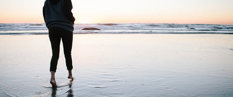 A woman dipping her toes in the water on a beach during sunset.