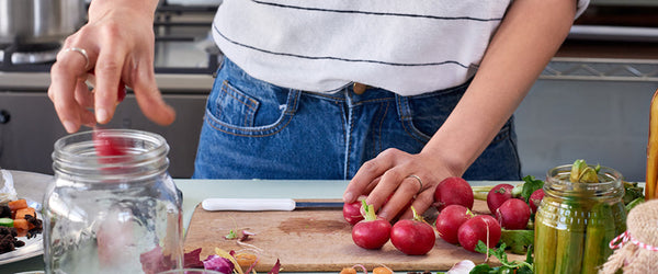 Midsection of a person cutting vegetables and putting them in a mason jar.