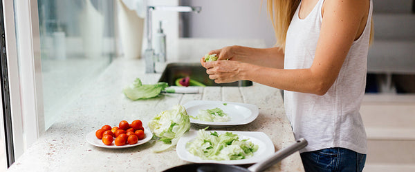 A view from the side of a woman making a salad at a kitchen counter.