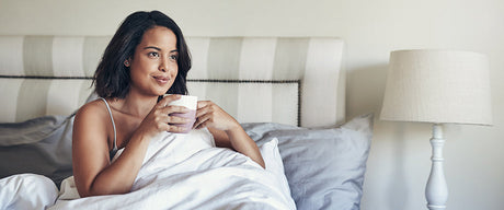 A woman sitting up in bed holding a coffee cup.