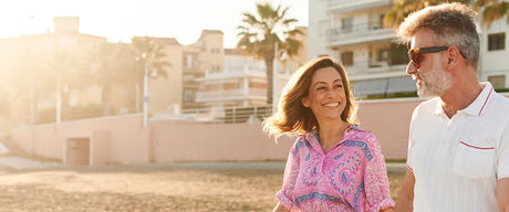 A mature couple smiling and walking on a beach.