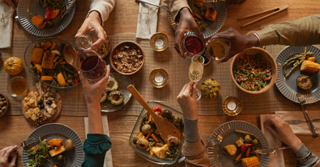 An overhead view of five people toasting with champagne and wine glasses over a holiday meal.