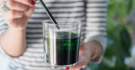 A woman adding liquid chlorophyll to a glass of water in her hand.