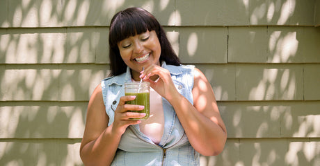 A smiling woman sitting outside with a green drink in her hand.