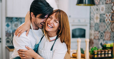 A man and woman hugging each other and smiling in a kitchen.