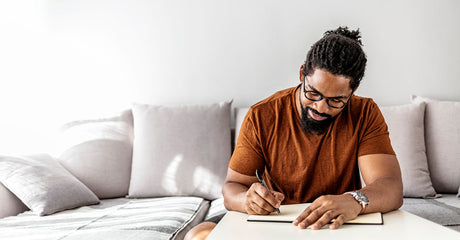 A man sitting on a couch and writing in a journal.