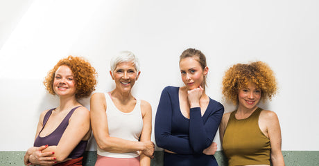 Four smiling women standing against a wall.