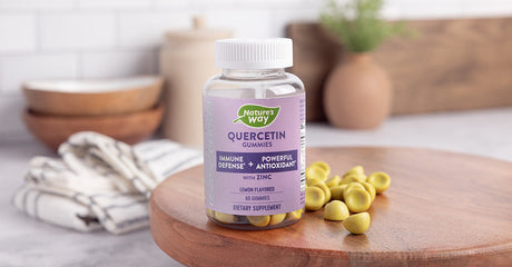 A bottle of Nature's Way Quercetin Gummies with Zinc sitting on a table next to several green gummies.