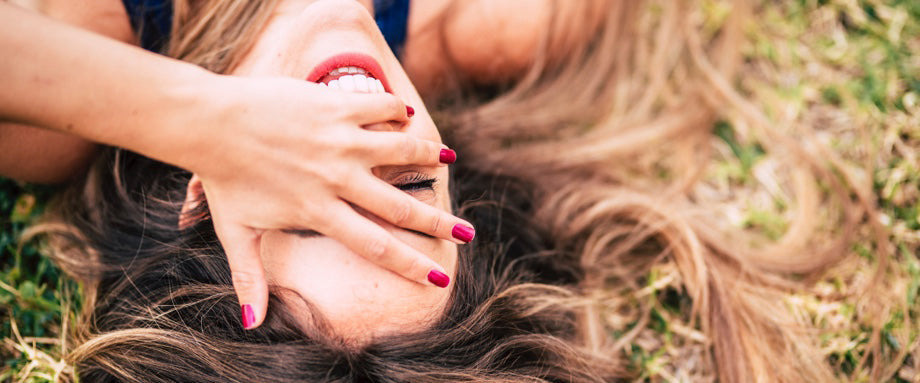 A woman laying in grass with her hand over her face.