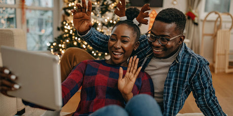 A man and woman sitting together on face time with holiday decor in the background.