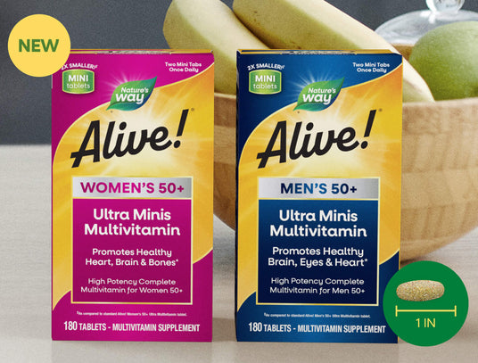 Two boxes of Nature's Way Alive! Ultra Minis Multivitamin in women's and men's 50+ sizes, shown side-by-side with bananas and a green apple in the background.