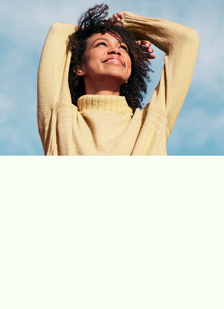 Woman in a yellow sweater smiling up at a blue sky