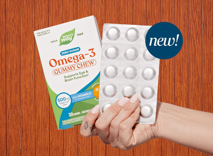 A hand holds a blister pack of Omega-3 gummy chew next to its retail box against a wood-grain background, with a blue 'new!' badge overlay.