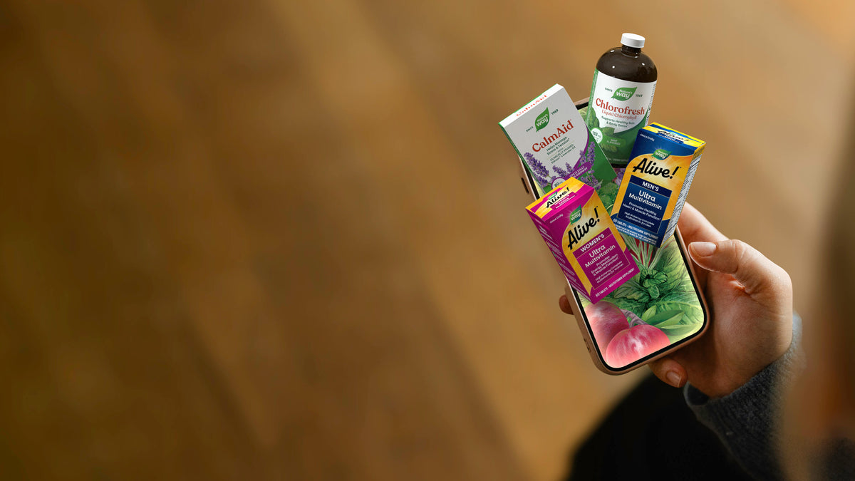 A hand holds a smartphone displaying a collage of wellness products against a warm, blurred wooden background.