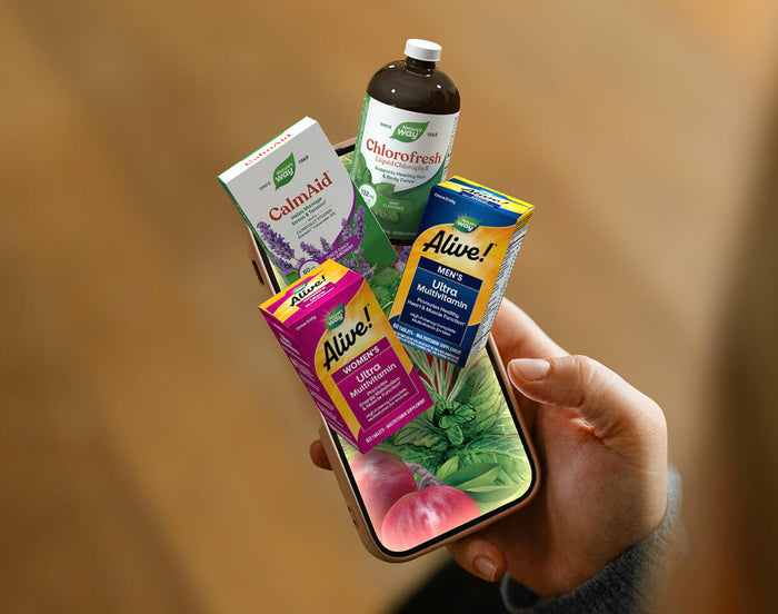 A hand holds a smartphone displaying a colorful herbal supplement bundle against a warm, blurred background.