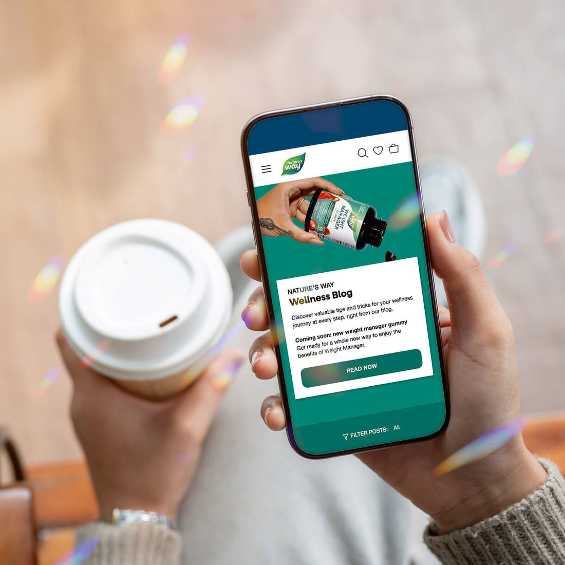 Person holding a smartphone with a Nature's Way Wellness Blog page displayed, next to a coffee cup.