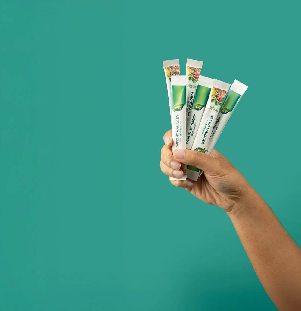 Hand holding multiple Weight Manager packets against a teal background