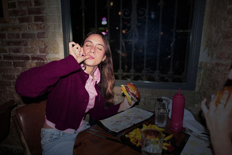 Woman sitting at a table with food and drinks, in a casual setting.