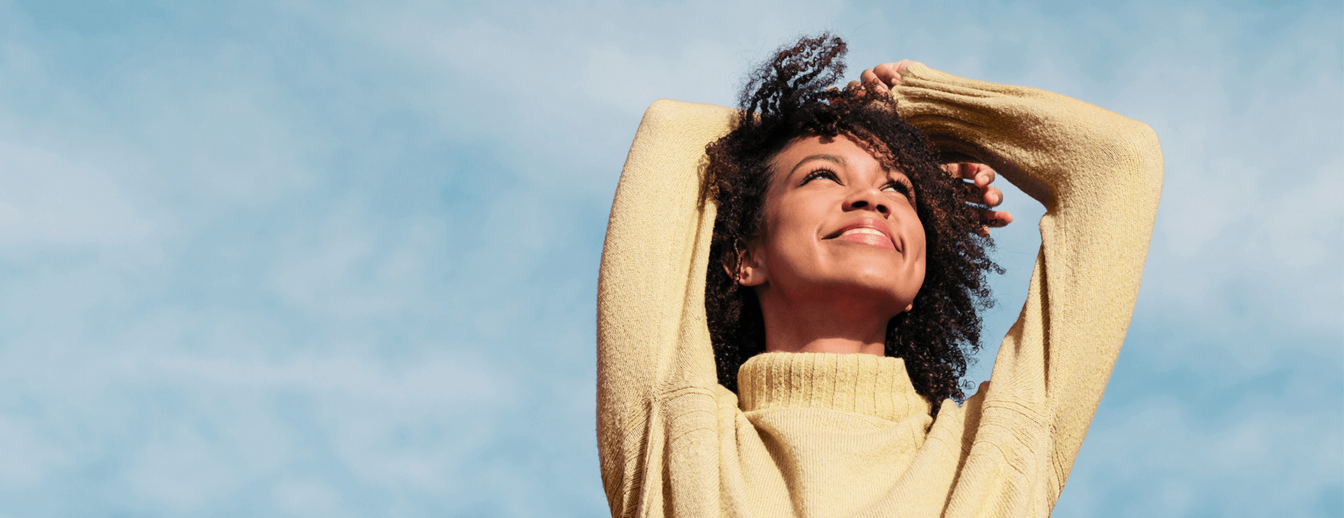 Woman in a yellow sweater smiling up at a blue sky