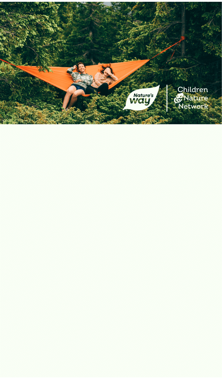 Two women sitting in an orange hammock in the forest