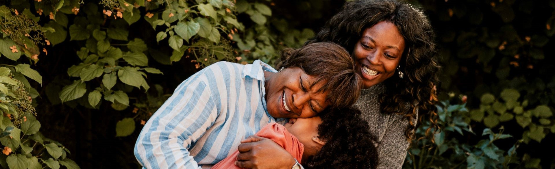 Two women hugging outdoors with greenery in the background