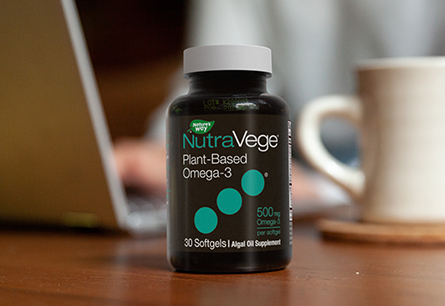 A bottle of Nature's Way NutraVege plant-based Omega-3, sitting in the foreground of a person on their laptop.