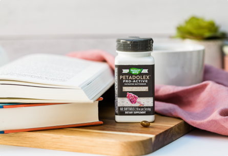 A bottle of Petadolex Pro Active sitting on a wooden surface next to books.