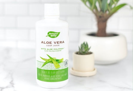 A bottle of Aloe Vera Leaf Juice sitting on a marble countertop with potted succulents in the background.