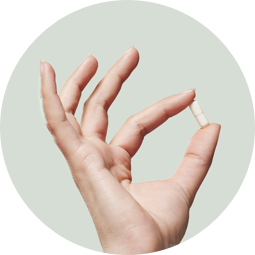 A hand holding a capsule between the thumb and forefinger.