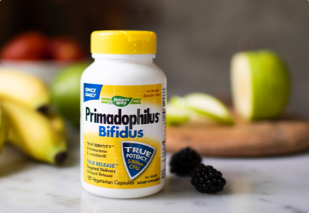 A bottle of Primadophilus Bifidus on a table next to blackberries, bananas, and a sliced green apple.