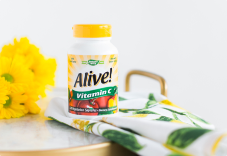 A bottle of Alive! Vitamin C sitting on a table next to a yellow flowers and a tea towel.