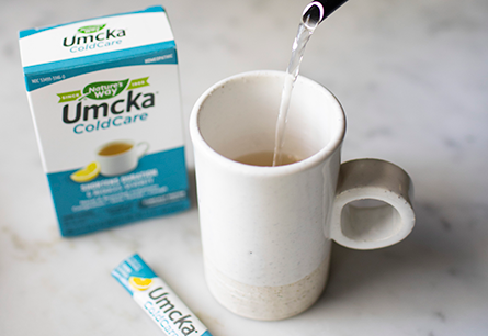 Pouring water into ceramic mug next to box of Umcka ColdCare hot drink packets.