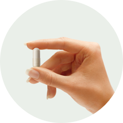 A hand holding a white capsule.