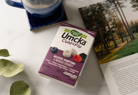 A package of Umcka Cold and Flu chewables laying next to a coffee cup and an open magazine.